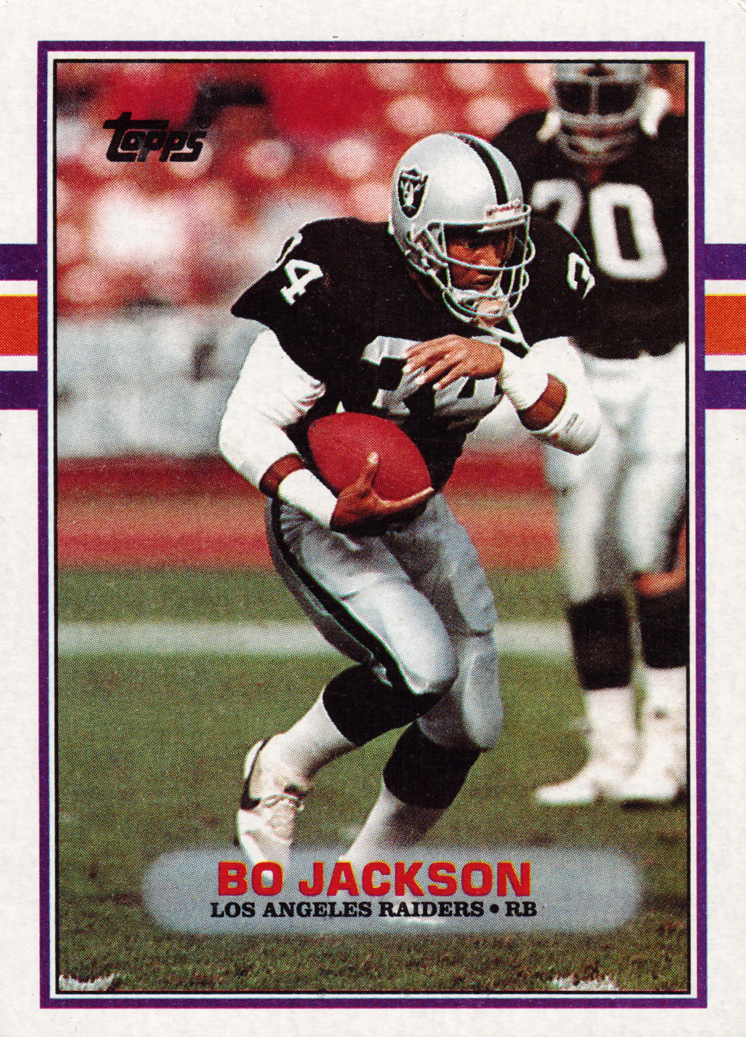 Front of 1989 Topps Bo Jackson #269, portrait-orientation front with purple border and orange/white stripe accents on left and right edges. Photo shows a Raiders player in black and…