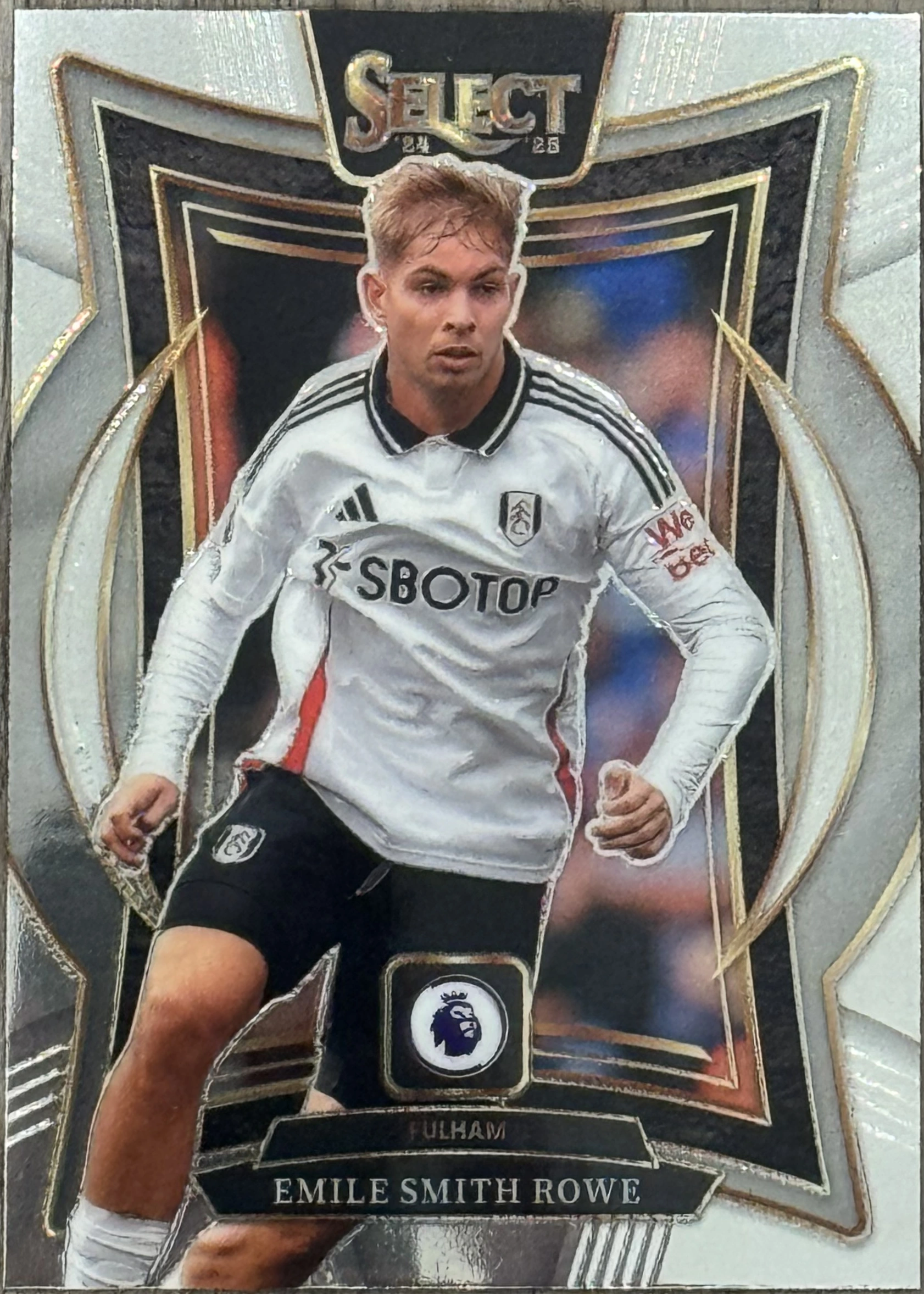 Front of 2024-25 Panini Select Premier League Soccer Emile Smith Rowe #No. 21 Terrace Silver, a soccer trading card featuring a player in a white Fulham jersey with black shorts, running. The card has a silver and gold border with a star-like…