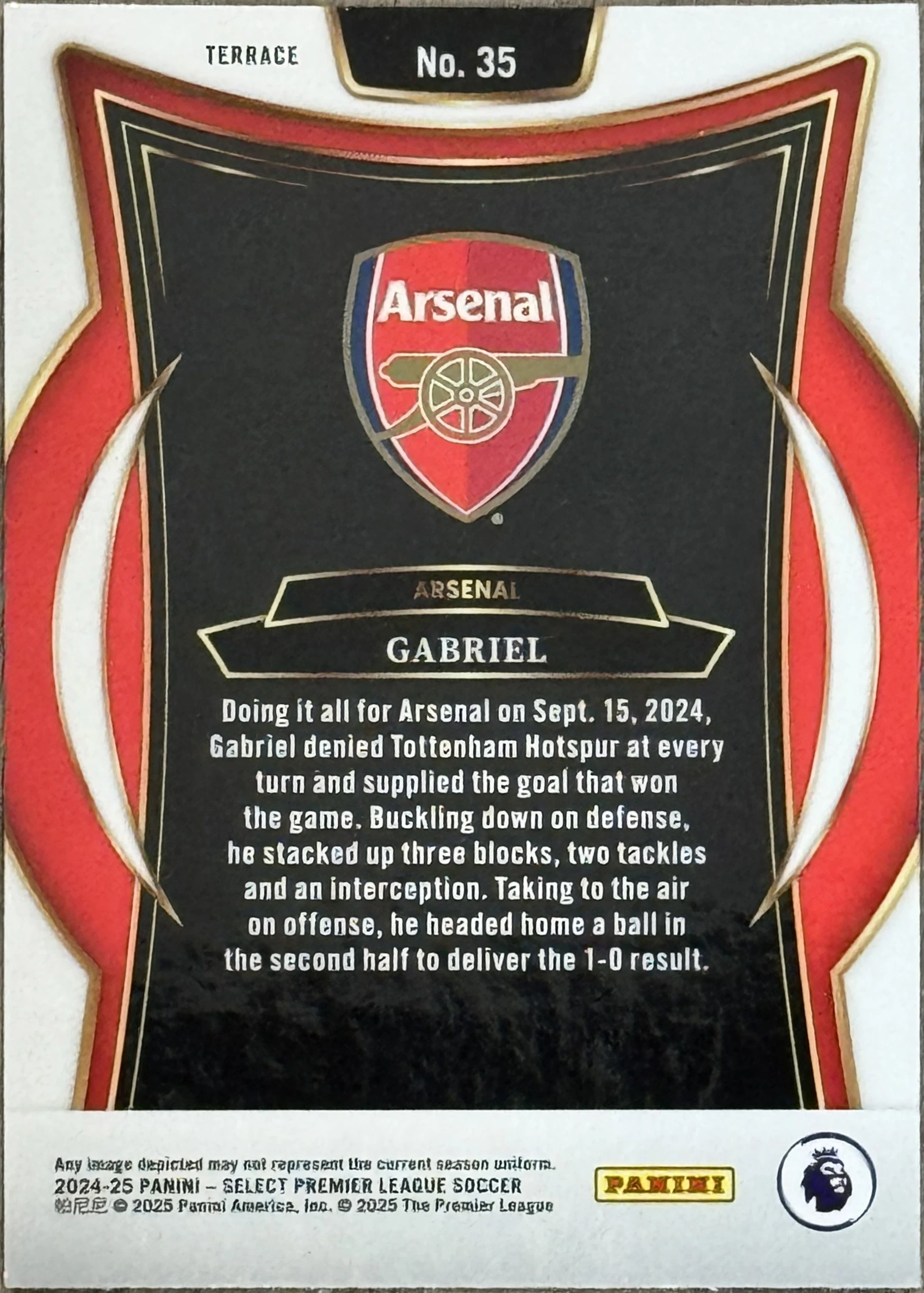 Back of 2024-25 Panini Select Premier League Soccer Gabriel #No. 35 Terrace, the back of a trading card featuring a die-cut patch of a black jersey with red and white trim. The patch includes the Arsenal club crest and a…