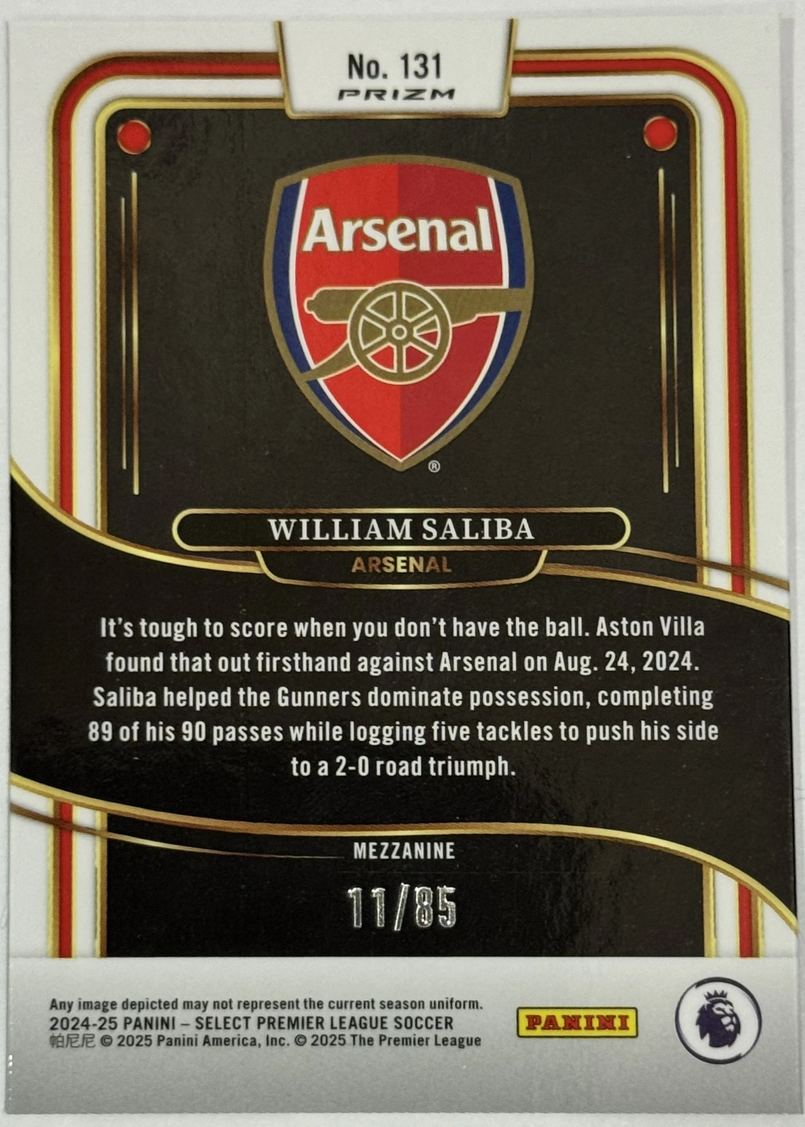 Back of 2024-25 Panini Select Premier League Soccer William Saliba #131 Mezzanine White Ice Prizm /85, serial numbered 11/85, the back of a trading card features a black background with gold and red border accents. At the top, a white tab displays 'No. 131' and the 'PRIZM'…