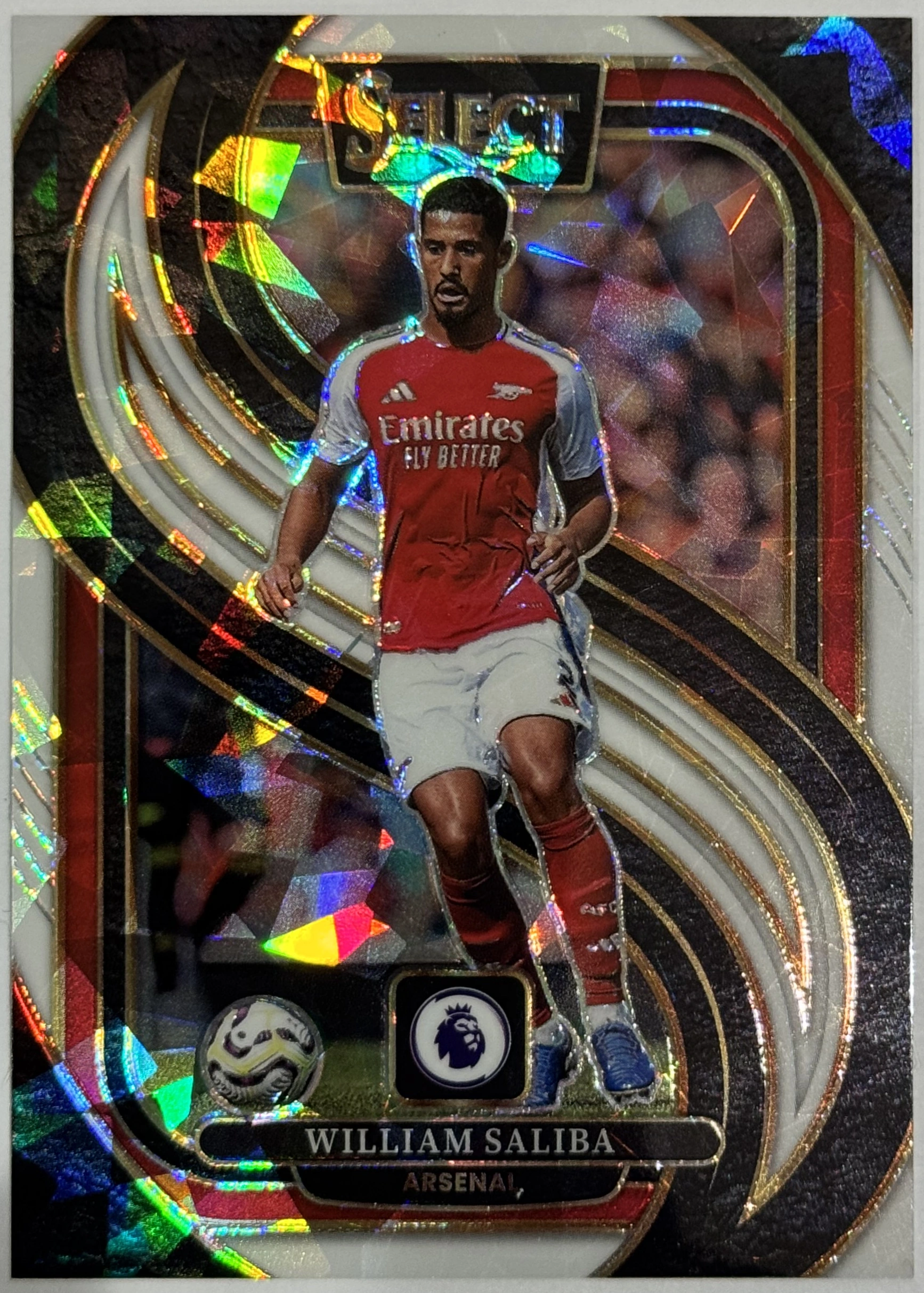 Front of 2024-25 Panini Select Premier League Soccer William Saliba #131 Mezzanine White Ice Prizm /85, serial numbered 11/85, a soccer card featuring a player in a red and white Arsenal jersey with the Emirates sponsor, white shorts, and red socks, set against a black, red…